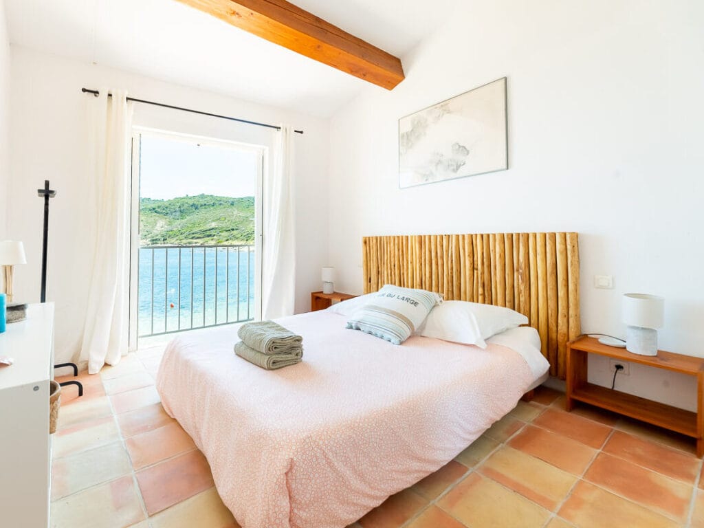Chambre lumineuse avec lit double, vue mer depuis la fenêtre.