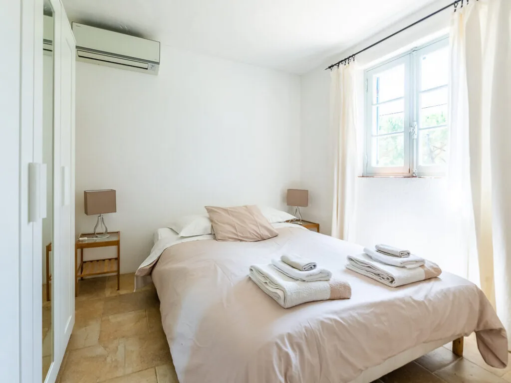 Chambre lumineuse avec lit double, linge de lit soigné et fenêtre ouverte sur l’extérieur.
