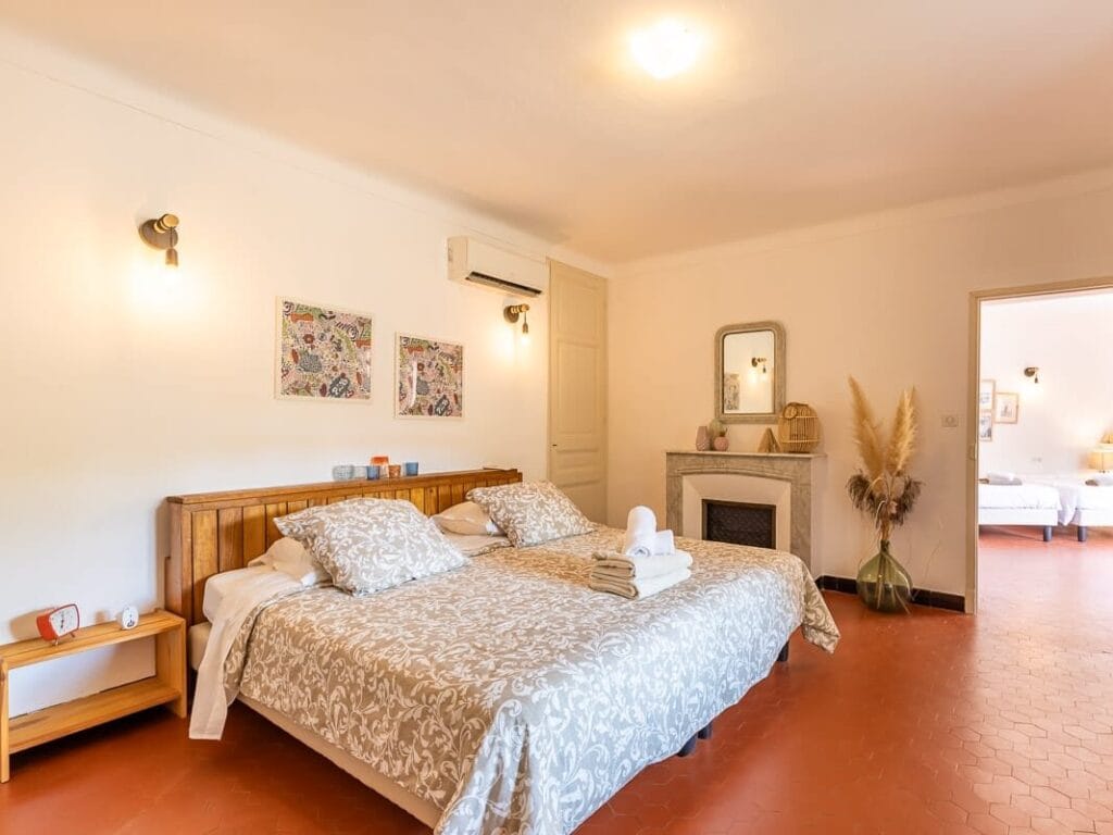 Chambre double lumineuse avec lit en bois, climatisation et décoration chaleureuse à La Ferme de l’Empereur en Provence