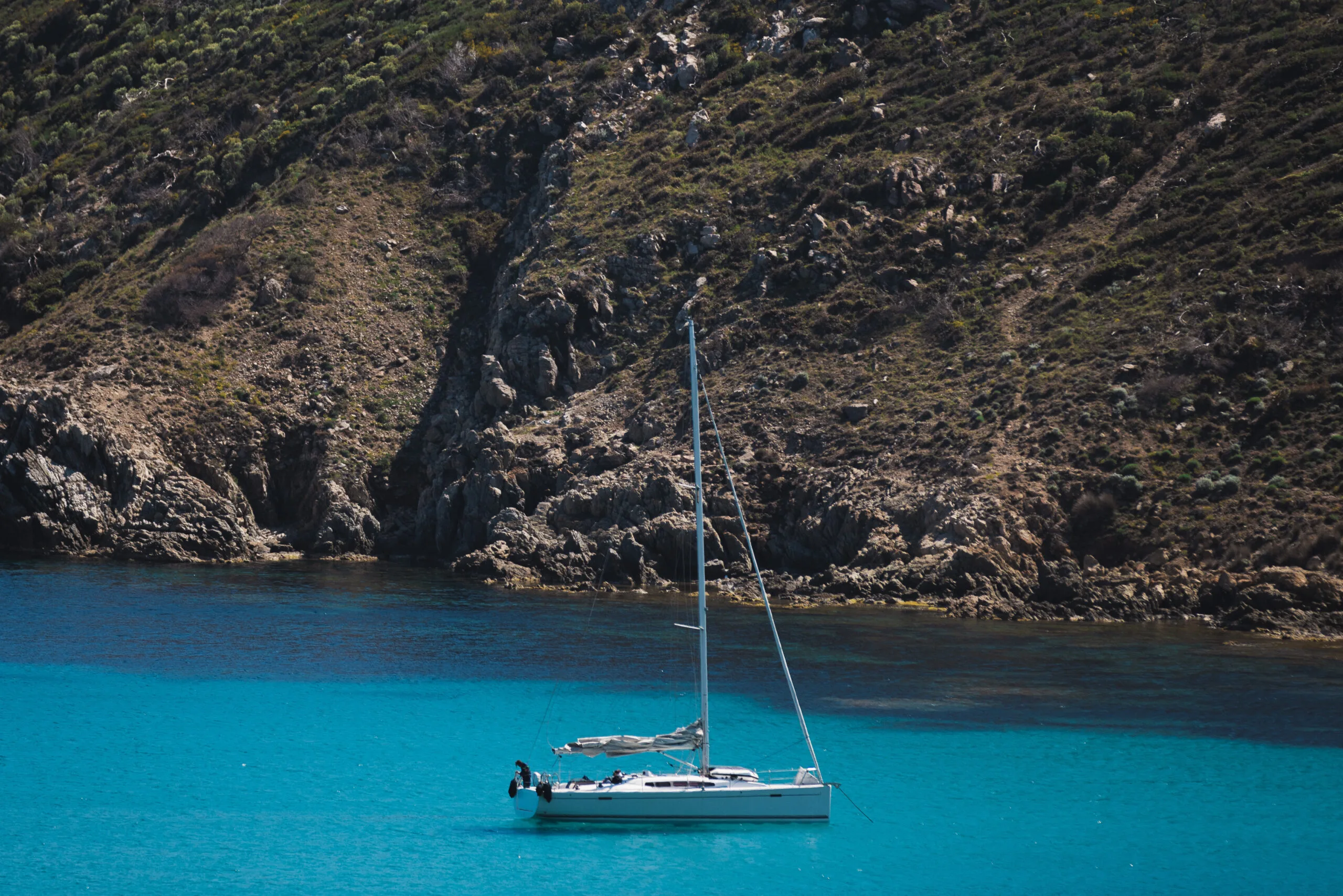 Voilier ancré dans les eaux turquoise au pied des falaises du Cap Taillat