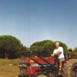Homme conduisant un tracteur rouge Case sur un chemin de terre, sous un ciel bleu clair.