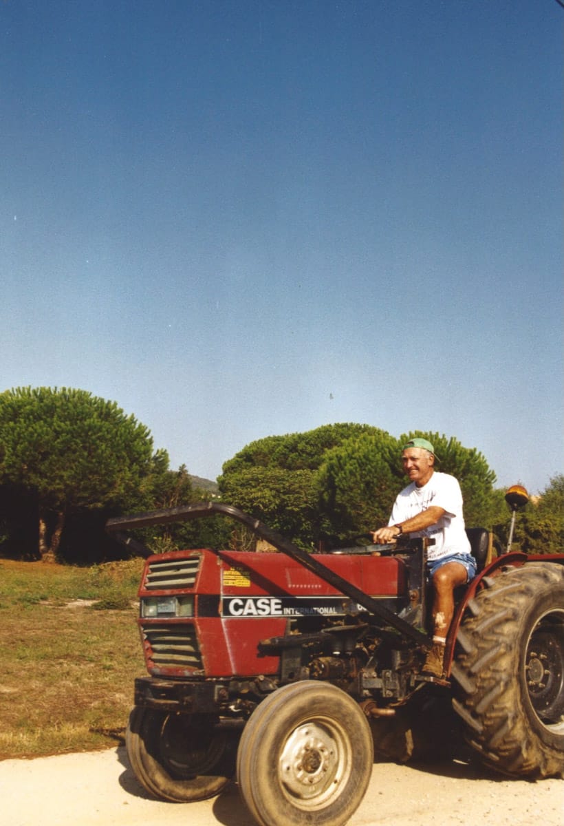 Homme conduisant un tracteur rouge Case sur un chemin de terre, sous un ciel bleu clair.