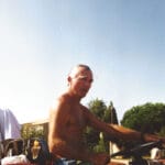 Homme torse nu conduisant un tracteur dans les vignes par temps ensoleillé.