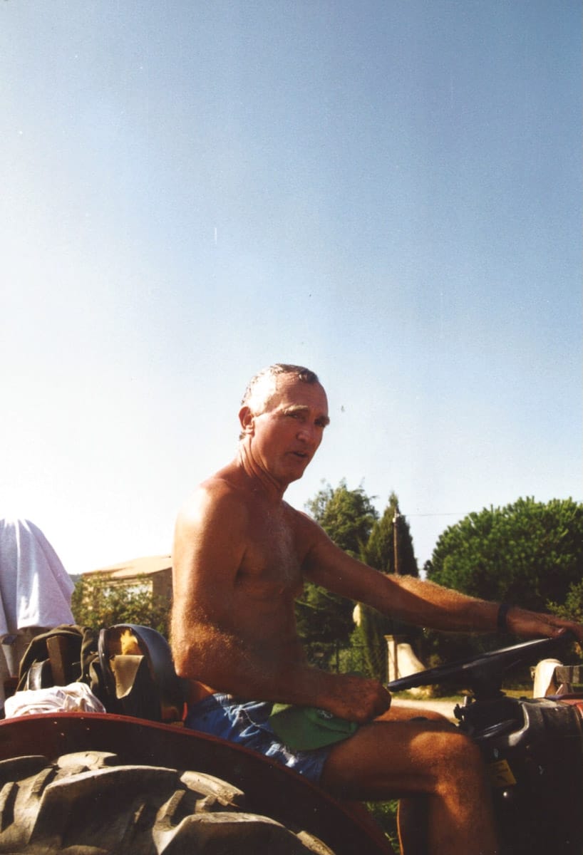 Homme torse nu conduisant un tracteur dans les vignes par temps ensoleillé.