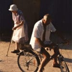 Homme âgé à vélo passant devant une femme âgée marchant avec une canne.