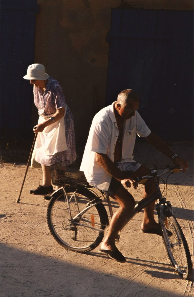 Homme âgé à vélo passant devant une femme âgée marchant avec une canne.