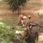 Homme conduisant un tracteur avec un enfant assis sur ses genoux, dans un champ.