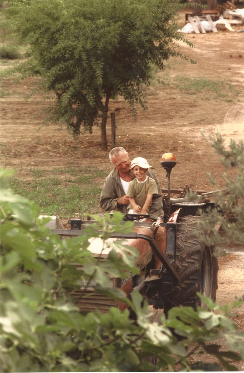 Homme conduisant un tracteur avec un enfant assis sur ses genoux, dans un champ.